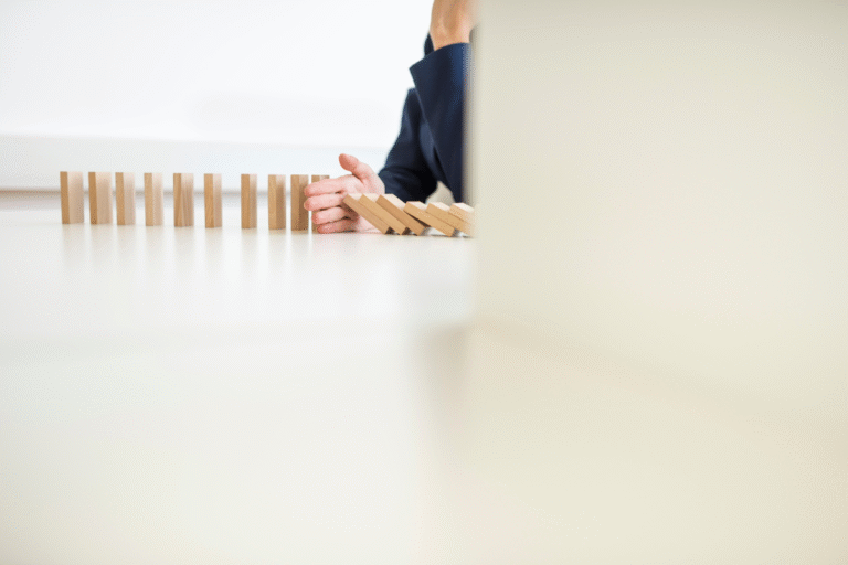 Main d'un investisseur stoppant la chute de dominos, symbolisant la gestion et la limitation des risques de requalification fiscale en Girardin industriel